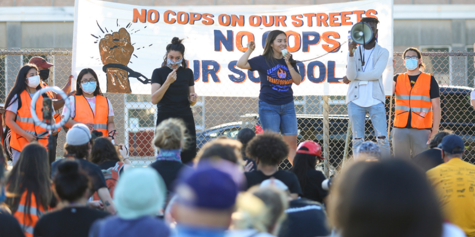 youth organizers on a stage in front of a banner that says no cops in our schools