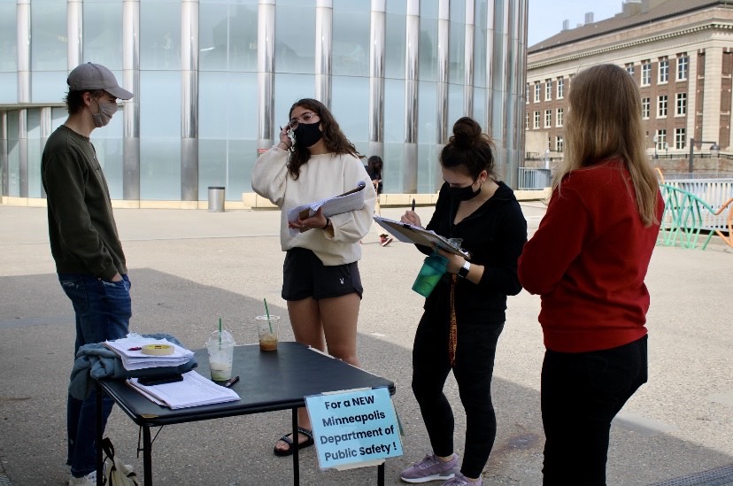 Young organizers tabling and collecting signatures at a table outside near a sign that says "for a new Minneapolis Department of Public Safety