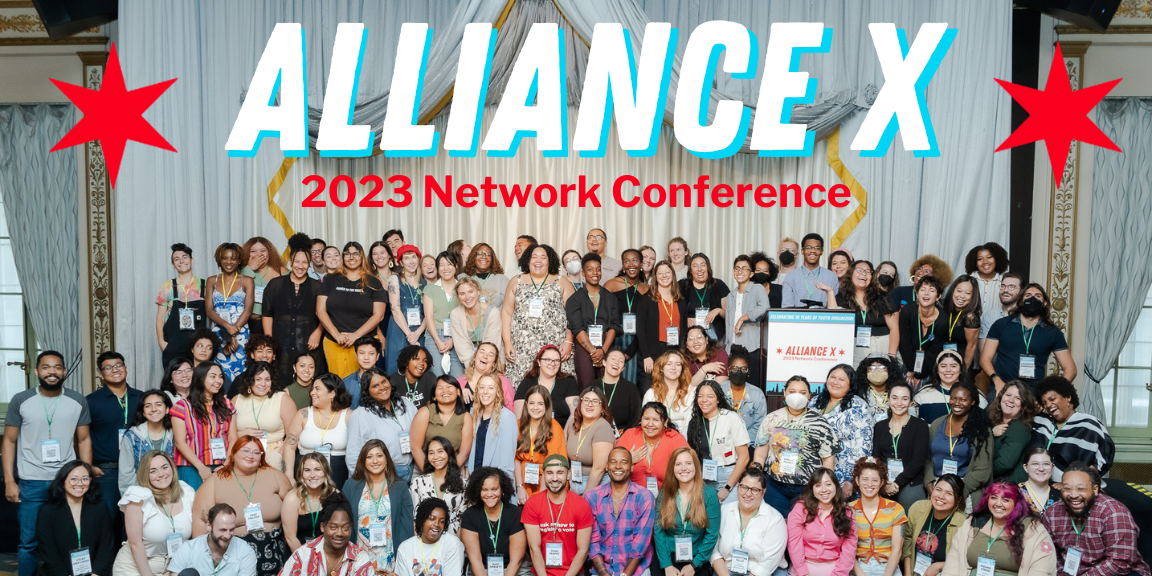Alliance X conference attendees posing together on a stage with "Alliance X 2023 Network Conference" at the top